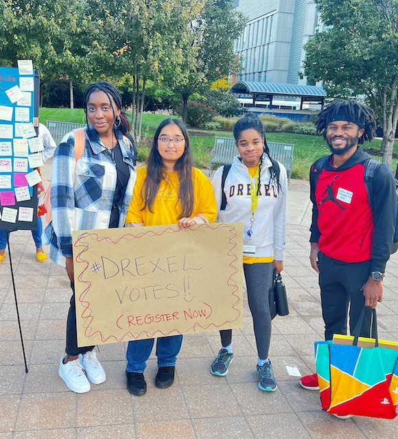Four students post for a photo at a voter registration table